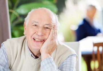 An elderly man at a table with his head leaning on one hand
